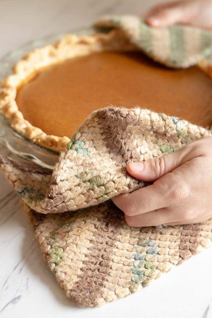 Hands with hot pats holding homemade pumpkin pie