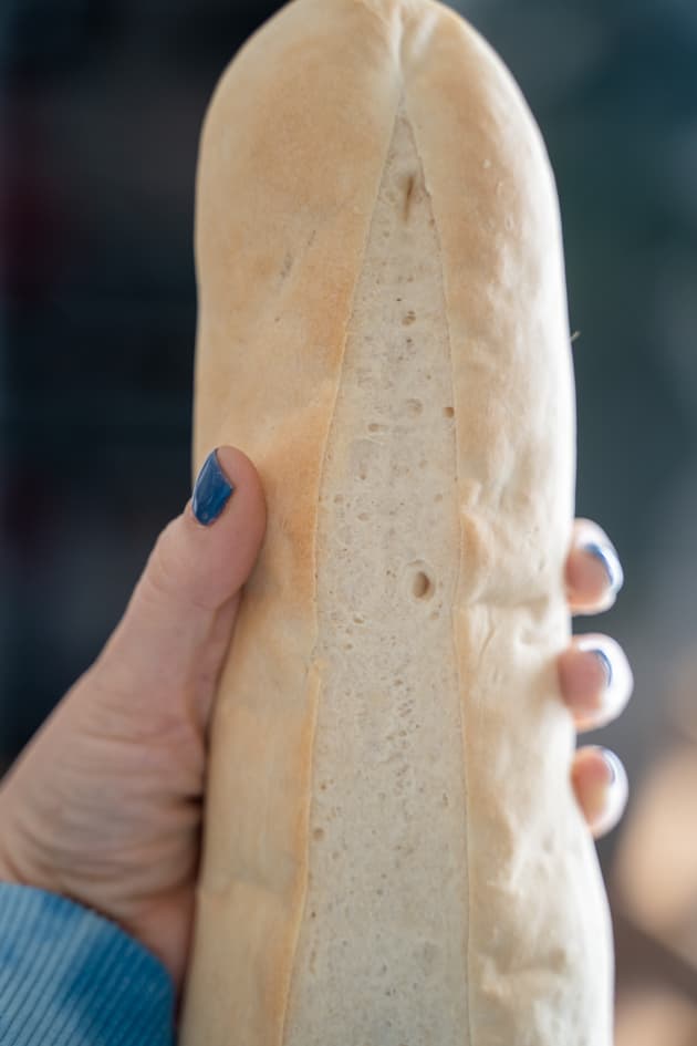 hand holding parbaked loaf of baguette