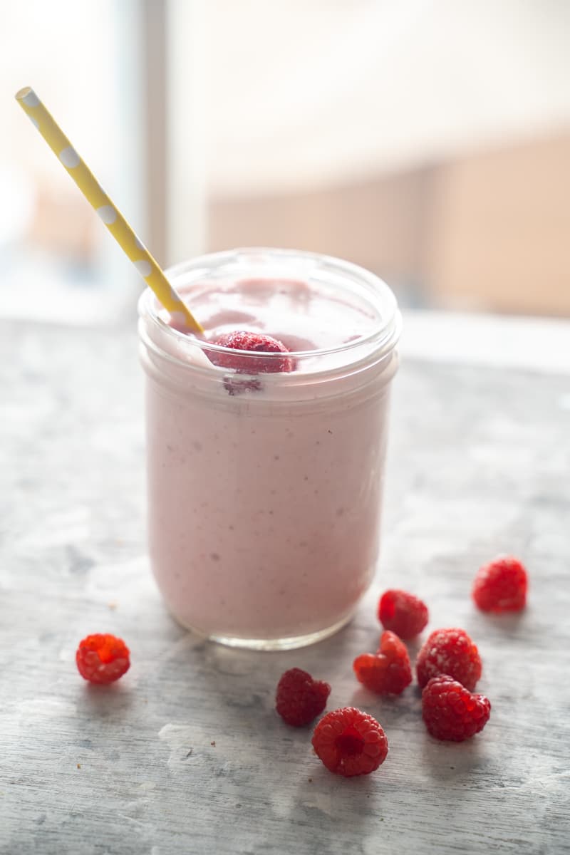 pink star smoothie with yellow straw and raspberries in front on granite backdrop with window behind